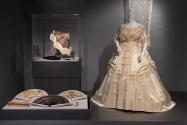 Silk evening gown, circa 1869, with lace shawl on wall, circa 1850, fans by J. Duvelleroy and unidentified designers, circa 1840-circa 1860, and parasols, 1840-1870