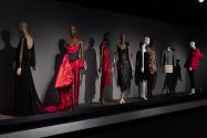 Dior + Balenciaga, Left to right: 2007.46.39 (black evening dress), 99.83.9 (corset evening ensemble), 2021.53.34 (red dress), 2001.45.1(black leather dress), 2008.60.1 (black one shoulder dress), 2005.23.1 (graffiti knit dress), 2019.21.1 (jacket), 2016.113.1 (red puffer coat)