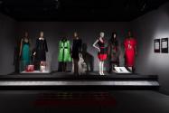 Platform featuring Twentieth century Latin American designers in the exhibition ¡Moda Hoy! Latin American and Latinx Fashion Design Today. From left to right: 78.147.3 (green gown), 93.129.10 (black dress), 98.102.5 (bag case), 77.190.28 (hat case), 2005.71.3 (green dress), 2005.48.8 (black dress), 2010.63.1 (black and red dress), 98.38.2 (coat), 2010.55.1 (red suit), 98.84.1 (sketch case)