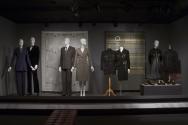 His and Hers_09 Left to right 78.57.6 (suit), 89.53.3 (velvet suit), 98.104.1 (textile wall), 93.54.12 (suit), 88.42.11 (knit skirt suit), 2005.40.15 (jacket), 98.20.7 (suit), 2005.25.1 (textile wall), 99.59.4 (dress), 91.256.1 (sweater), 2005.40.18, 2003.96.1, 2006.34.2 (shoes case) 
