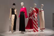 YSL+Halston_40 Left to right  92.140.1 (black and ivory pantsuit), 82.99.1 (pink and black gown),  91.185.2 (red strapless gown),80.128.10 (red white stripe dress), 2007.56.16 (ruffle top and black skirt hidden),  2014.38.2 (ivory evening dress)