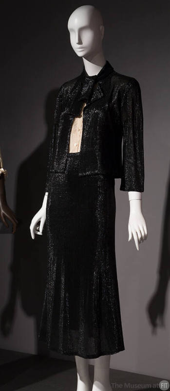 Black suit with fitted, tie collar jacket, calf length A-line skirt and white button front shir…