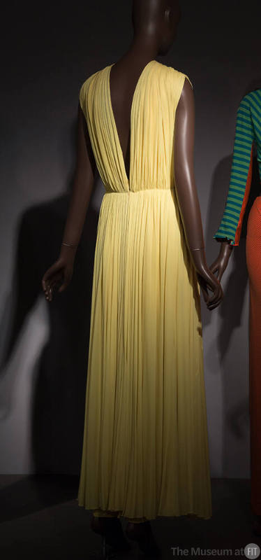 Back view of yellow sleeveless evening gown with deep V-back, gathering at waist and shirring o…