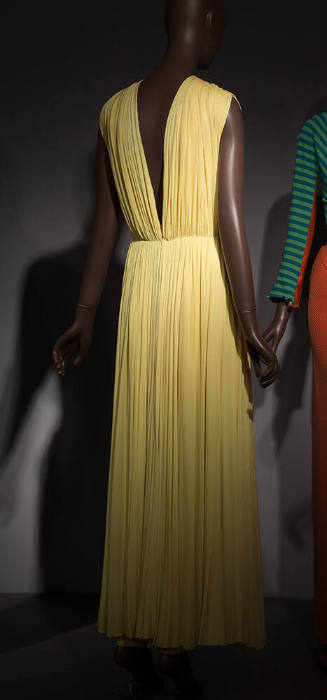 Back view of yellow sleeveless evening gown with deep V-back, gathering at waist and shirring o…