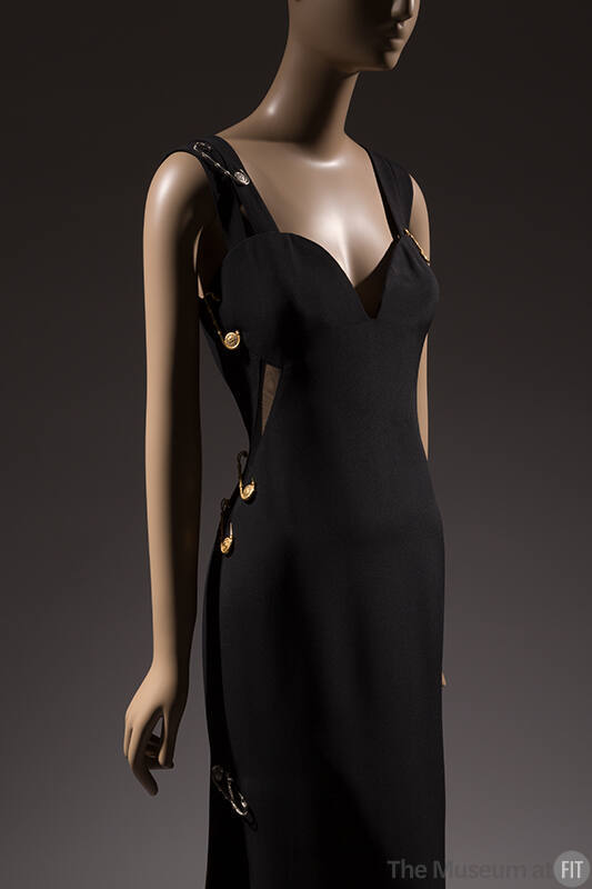 Black sleeveless evening dress with sweetheart neckline and oversize gold safety pins attached …