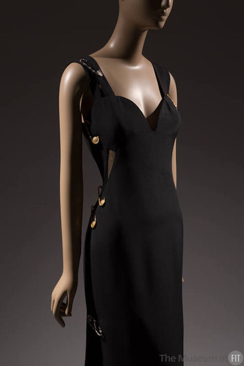 Black sleeveless evening dress with sweetheart neckline and oversize gold safety pins attached …