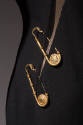 Detail view of black evening dress showing two gold safety pins with Medusa head Versace logo