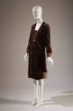 3/4 view of black dress with multicolor geometric velvet pattern, pink ribbon and fur trim