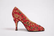 View of single red pump showing floral brocade and black and gold bead embroidery