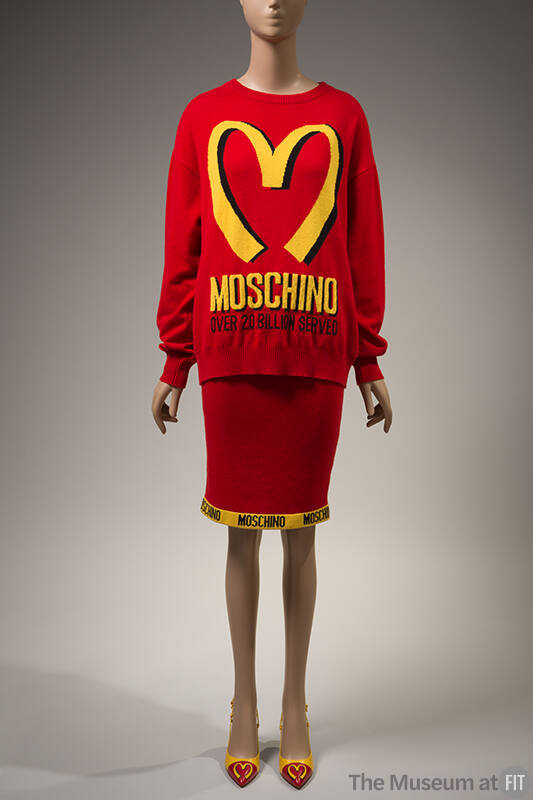 red sweater with yellow "Moschino Over 20 Billion Served" print and large yellow "M" and machin…