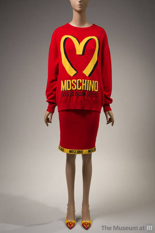 red sweater with yellow "Moschino Over 20 Billion Served" print and large yellow "M" and machin…