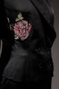 Detail view of black evening pantsuit showing embroidered pink rose on left side of jacket with…