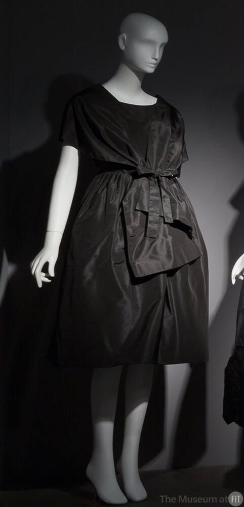 Black cocktail dress with fitted bodice, back wrap styling, dome skirt, and bow at waist