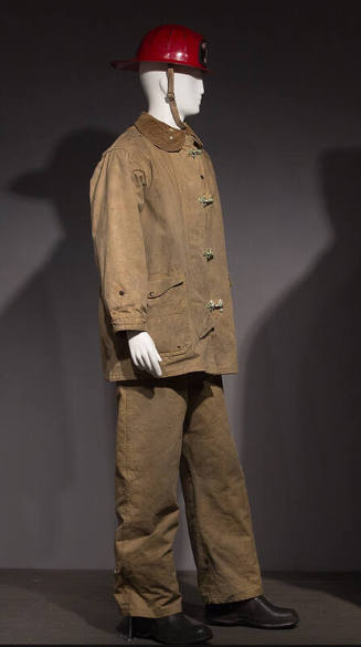 Fireman's protective uniform coat and pants in heavy tan canvas with metal closures, dressed wi…