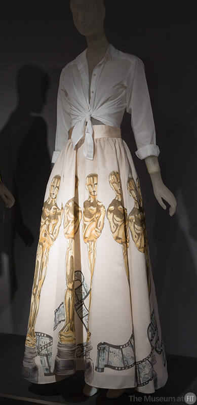 White button front shirt tied at the waist and white ankle length bell skirt painted with large…