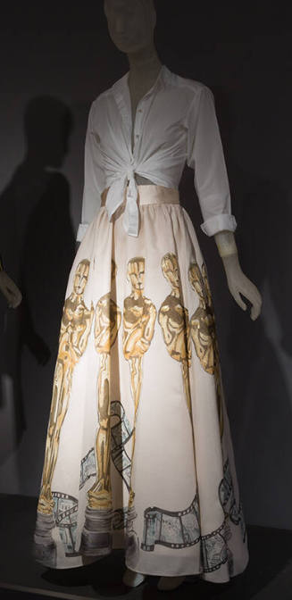 White button front shirt tied at the waist and white ankle length bell skirt painted with large…