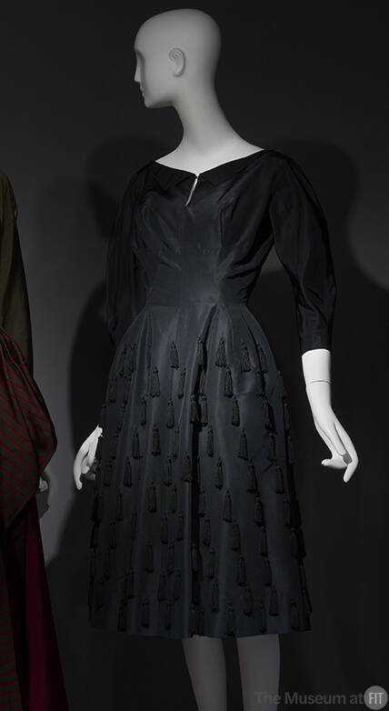 Black silk boat neck dress with 3/4 sleeves, multiple fringe tassels on full to-the-knee skirt