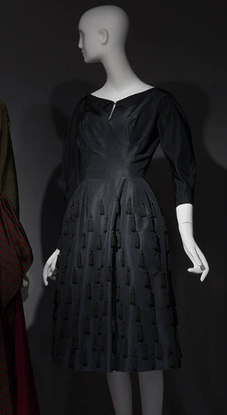 Black silk boat neck dress with 3/4 sleeves, multiple fringe tassels on full to-the-knee skirt
