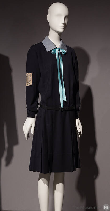 Navy blue uniform dress with long sleeves, light blue collar with aqua blue ribbon bow tied at …