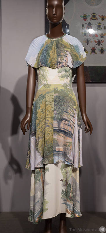 Off-white ankle length dress with blue, green, yellow and pink landscape print, pleated capelet…