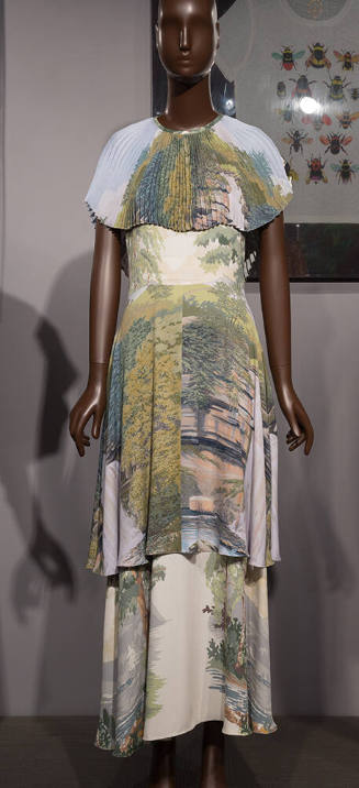 Off-white ankle length dress with blue, green, yellow and pink landscape print, pleated capelet…