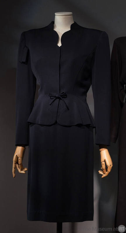 Navy blue suit:  jacket with scallop cut V-neck, shoulder pads, and below knee length straight …