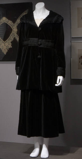 Black velvet suit of knee length jacket with sailor collar, braid trim at high waist and cuffs …