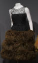 Sleeveless black lace evening dress with triple tier of long brown ostrich feathers on full ski…