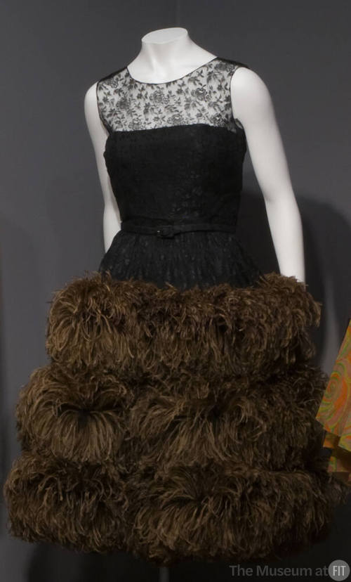 Sleeveless black lace evening dress with triple tier of long brown ostrich feathers on full ski…