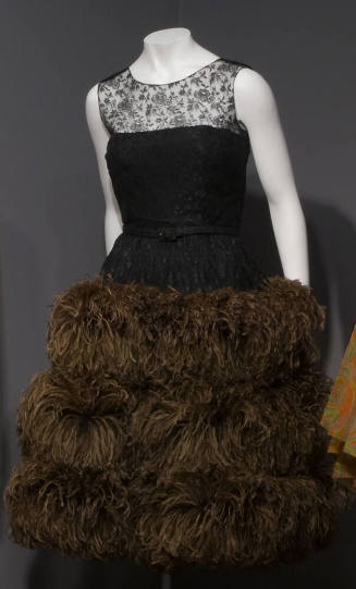 Sleeveless black lace evening dress with triple tier of long brown ostrich feathers on full ski…