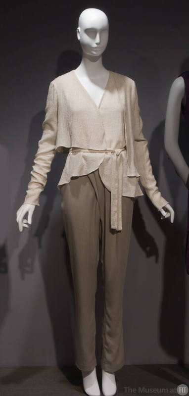 Off-white long sleeve wrap top with asymmetric hem and tie sash, beige pants with pleated front