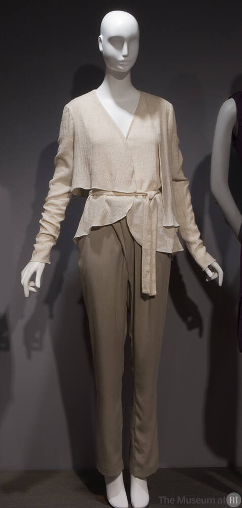 Off-white long sleeve wrap top with asymmetric hem and tie sash, beige pants with pleated front