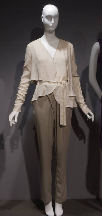 Off-white long sleeve wrap top with asymmetric hem and tie sash, beige pants with pleated front