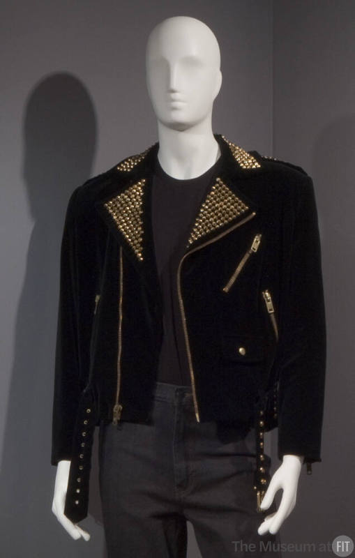 Black motorcycle style jacket with gold nail heads on notched lapels, gold zippers and studs on…