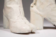 Detail view of white painted boots showing split toe, cylindrical heel and cracked white paint …