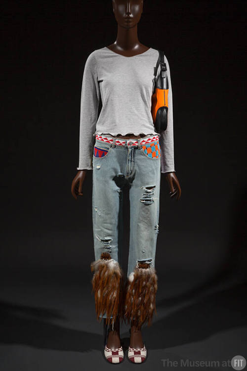 Ensemble of grey long sleeve top, distressed blue jeans with brown feathers at lower leg, orang…