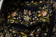 Detail view of man’s navy blue coat showing floral embroidery in greens, yellows, pinks, white …