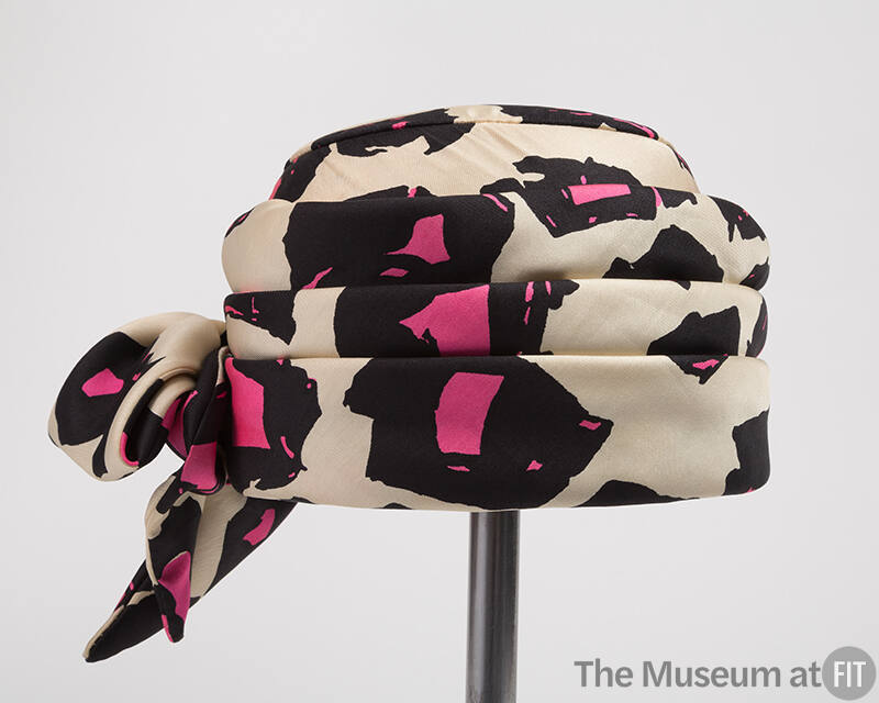 White pill box hat printed with black and pink abstract shapes and large bow on left side