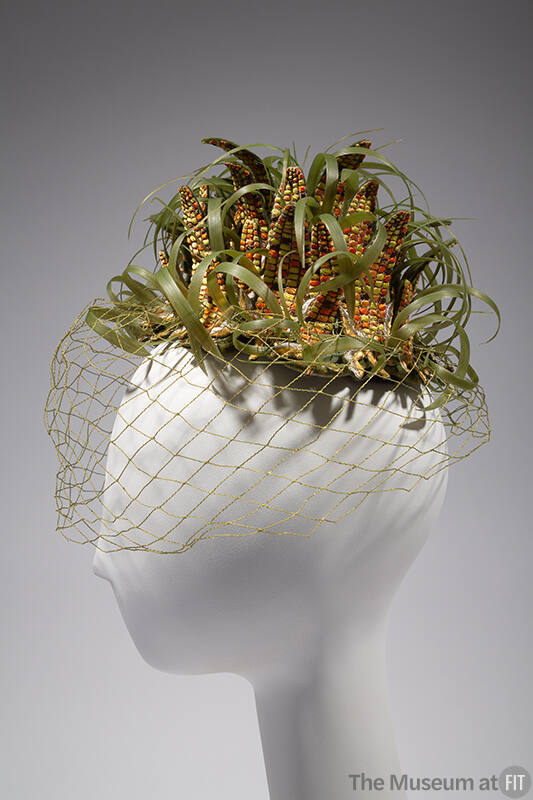 Small hat in the shape of multiple ears of corn and husks with green net face veil