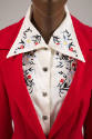 Detail view of red dress bodice showing blue, yellow, black and red floral embroidery on white …