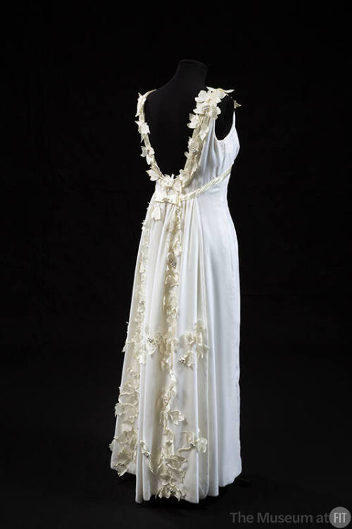 Back view of white sleeveless floor length evening dress with low scoop back trimmed with white…