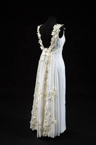 Back view of white sleeveless floor length evening dress with low scoop back trimmed with white…
