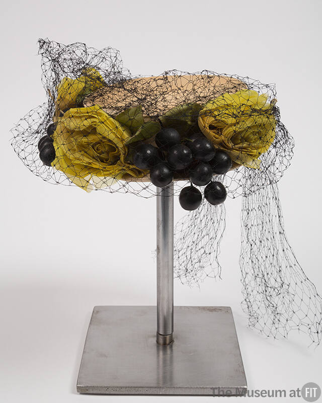 Off-white circular hat with large yellow/green roses, green leaves, and black grapes covered wi…