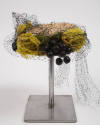 Off-white circular hat with large yellow/green roses, green leaves, and black grapes covered wi…