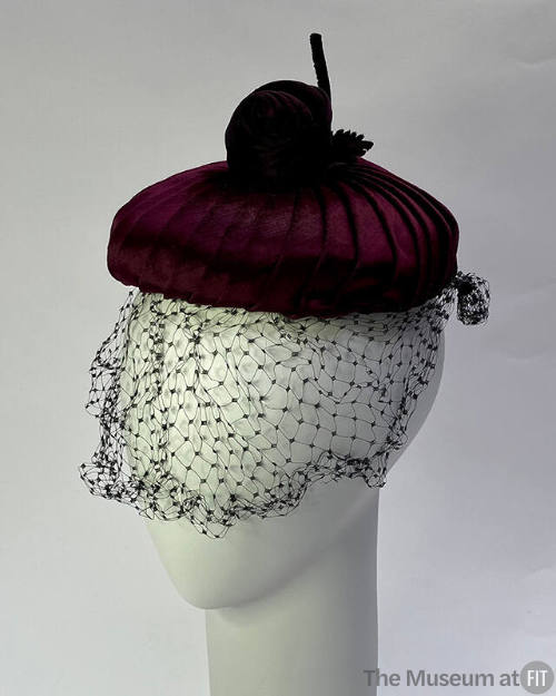 Small circular burgundy velvet hat topped with velvet rose; net face veil 