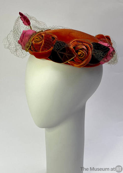 Red velvet hat encircled with pink satin and red velvet roses and green velvet leaves