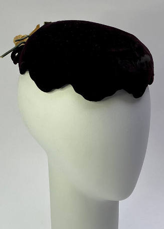 Small dark purple hat with scalloped edge and cream floral trim at center back