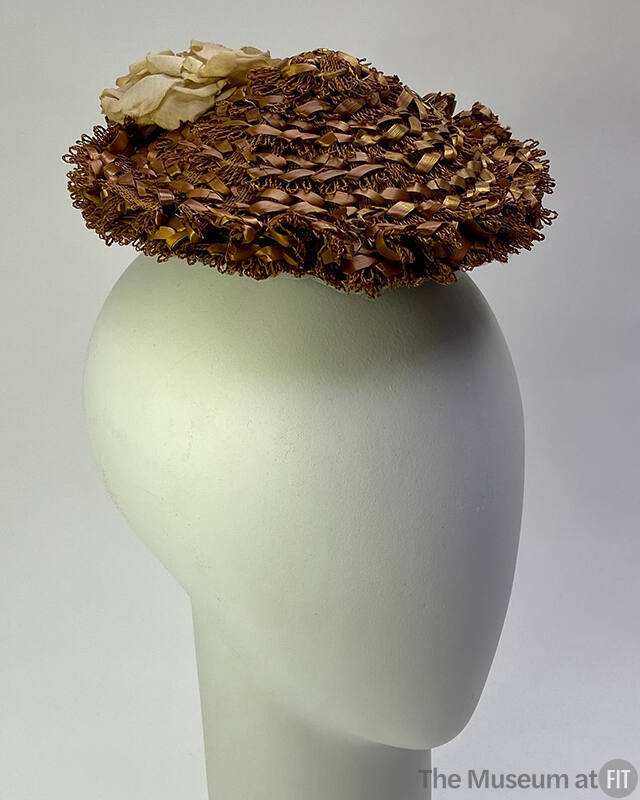 Small light brown toque hat made of loops of threads with ribbon woven through in concentric ri…