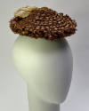 Small light brown toque hat made of loops of threads with ribbon woven through in concentric ri…