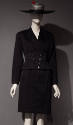 Black suit jacket and knee length skirt styled with black and white striped hat